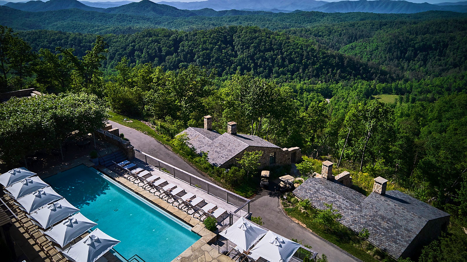 An aerial view of Blackberry Mountain resort, with its outdoor pool, set against the backdrop of the deep green, forested Smoky Mountains